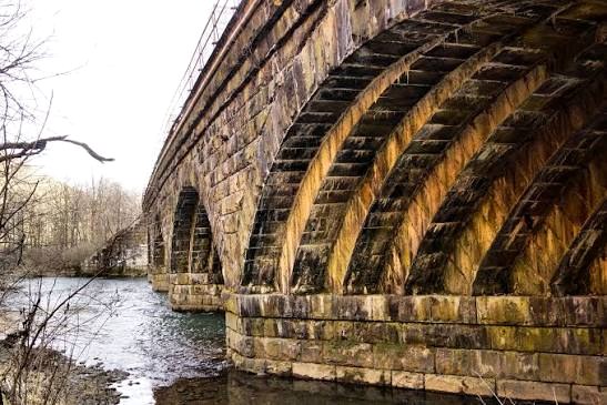The old stone arch railroad bridge crossing the Little Juniata, its gold-stained arches standing over the winter river